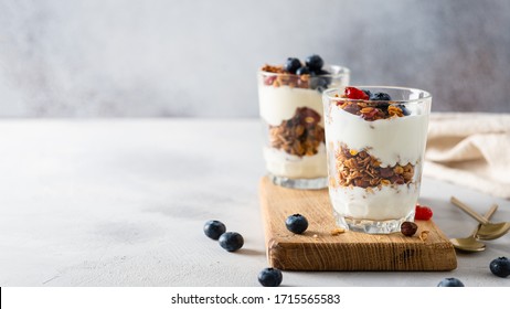 Crunchy honey granola with yogurt in a glass on gray background. Dry breakfast cereals with flax seeds, cranberries and nuts. Healthy, vegeterian fiber food. Banner. Menu, recipe. Copy space for tex