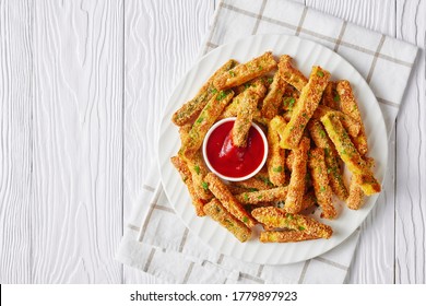 crunchy zucchini sticks breaded with panko breadcrumbs, parmesan cheese, spices on a white plate with ketchup on a wooden table, view from above, flat lay, free space