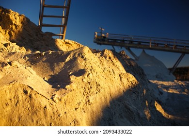 Crushed rock and stone dust in sunset lighting, close-up, the blurry dark silhouettes of rock crushing equipment in the background.