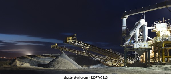 Crusher plant, illuminated by spotlights during operation at night, panorama. Mining industry.