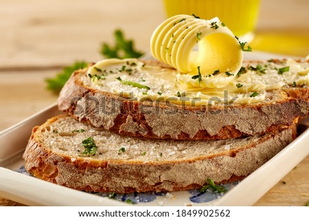 Crusty slices of fresh buttered rye bread garnished with chopped parsley and a butter curl in close up on a plate or tray