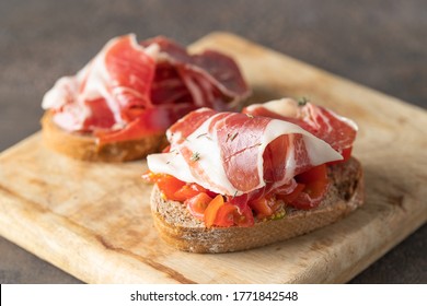 Crusty toast with fresh tomatoes and cured ham. Delicious appetiser Italian prosciutto and Spanish Iberian ham snack