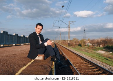 Cry, drama concept. Depressed young sad businessman sitting on suitcase head in hands on the railway platform alone,