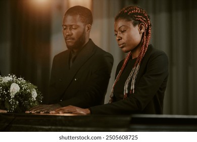 Crying African American woman and doleful man touching coffin - Powered by Shutterstock