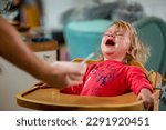 crying and angry little girl sitting in a high chair and refusing a bowl of food, period of defiance, patient and respectful parents
