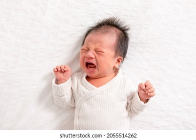 Crying And Angry Newborn Baby Boy Lying On White Bed At Home.Infant Baby Screaming Very Hungry Or Stomach Pain. Sick Asian Baby Crying And Having Fever. Tired Baby Crying Concept