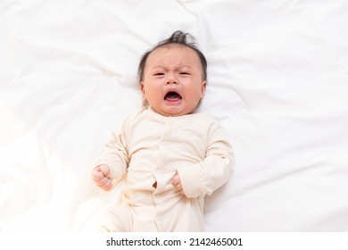 Crying And Angry Newborn Baby Boy Lying On White Bed At Home.Infant Baby Screaming Very Hungry Or Stomach Pain.sick Asian Baby Crying And Having Fever.Tired Baby Crying Concept