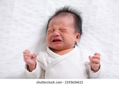 Crying And Angry Newborn Baby Boy Lying On White Bed At Home.Infant Baby Screaming Very Hungry Or Stomach Pain. Sick Asian Baby Crying And Having Fever. Tired Baby Crying Concept