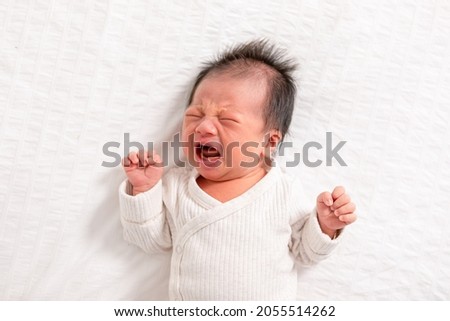 Crying and angry Newborn baby boy lying on white bed at home.Infant baby screaming very hungry or stomach pain. sick asian baby crying and having fever. Tired baby crying concept
