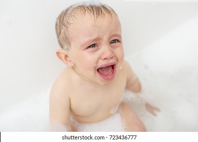 Crying baby by in a bathtub. Infant kid sreaming while taking a bath.