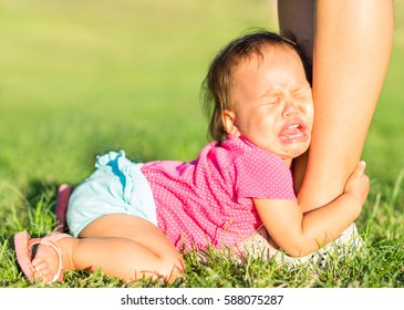 Crying baby girl holding onto mothers leg outdoors. - Powered by Shutterstock