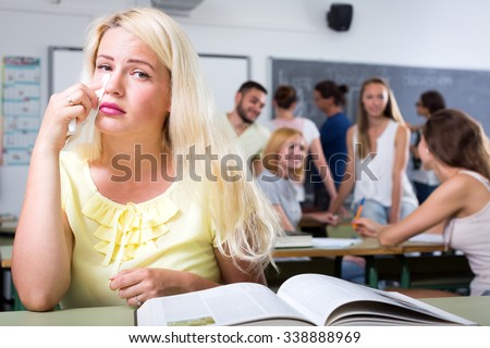 Crying beautiful blonde sitting in college classroom at the table near a textbook