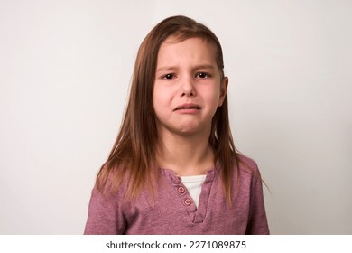 Crying child girl against white background with copy space. Portrait of a sad baby girl with tear drops on eyes, close-up