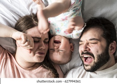 A crying couple and a little baby in bed at home