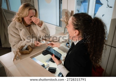 Crying customer feeling sadness while paying for a purchase with euro cash to a smiling cashier in a retail store