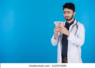 Crying Doctor In The White Coat Hold Egyptian Pounds Counts The Few Salary With Sad Face Emotions On Blue Background.