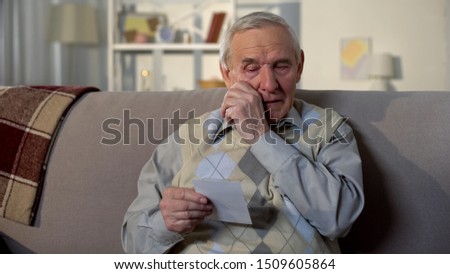Crying elderly man looking at photo, remembering old lost friend, memories