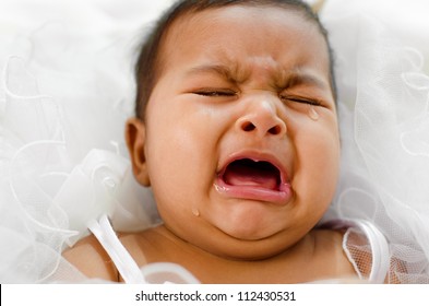 Crying Indian baby girl lying on bed