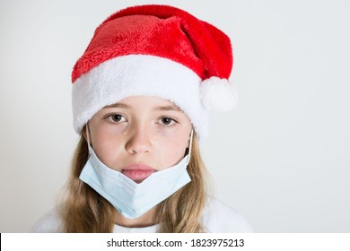 Crying Kid With Red Santa Claus Hat And Mask Isolated On White Background. Sad Child Face With Surgical Mask. Christmas Covid 19 Concept, Isolated White Background Copy Space.