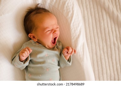 Crying Little Baby Lying In Crib Try To Sleep With Stomach Ache And Colic Pain In Room In Bed Close. Top View. Childhood. Sick Little Newborn Child Yawn. 