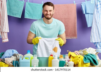 Crying Man In Blue T-shirt Holding His Favourite T-shirt With Spot Of Grease. Emotional Guy Is Unhappy As He Has Found Stain On His Clothes. Isolated Blue Background, Studio Shot.