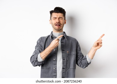 Crying man whining and complaining, pointing fingers right at sad news, standing miserable on white background