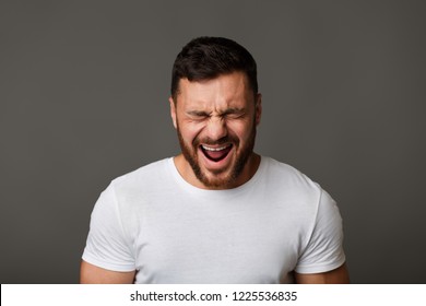 Crying man. Young guy in white t-shirt grimacing on gray studio background - Shutterstock ID 1225536835