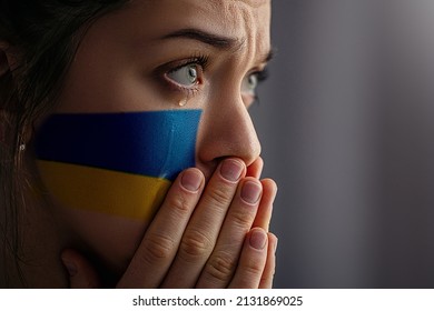 Crying sad feared depressed frightened emotional woman with Ukraine flag on face in the dark. Stop war between Russia and Ukraine. Stay with Ukraine. Pray and hope for peace and world. Copy space 