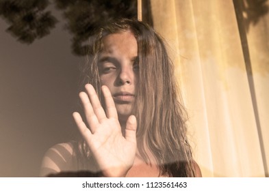 Crying Sad Little Girl Looking Out The Window.Anxious Child Waiting Near Window Glass With Reflection.Vintage Ton