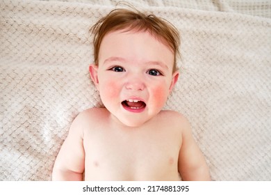 Crying Screaming Toddler Baby Boy Is Lying On The Bed. Unhappy Child Close-up On A White Blanket. Kid Aged One Year