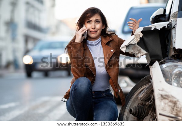 Crying woman talking on mobile phone and\
calling for road assistance after a car accident.\

