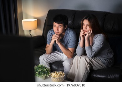 Crying Young Couple Watching Romantic Movie TV On Sofa At Night