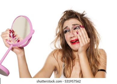 Crying Young Woman With Bad Makeup And Messy Hair Looking At Herself In The Mirror