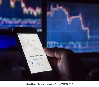 Crypto currency day trader holding mobile phone looking at charts in front of computer screens in dark, Vienna Austria 25-3-2018 - Shutterstock ID 1054200746