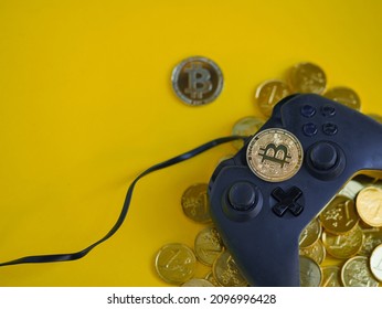 Crypto gaming. Play for earn concept. Top view of a video game controller joystick with focus on a bitcoin cryptocurrency coin on top,  gold coins underneath. Copy space. Vivid yellow background. - Shutterstock ID 2096996428