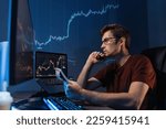 Crypto trader freelancer sitting at table with notepad late night. Noting down info after checking ico and trading market dynamics on his personal computer with candlestick chart on display 
