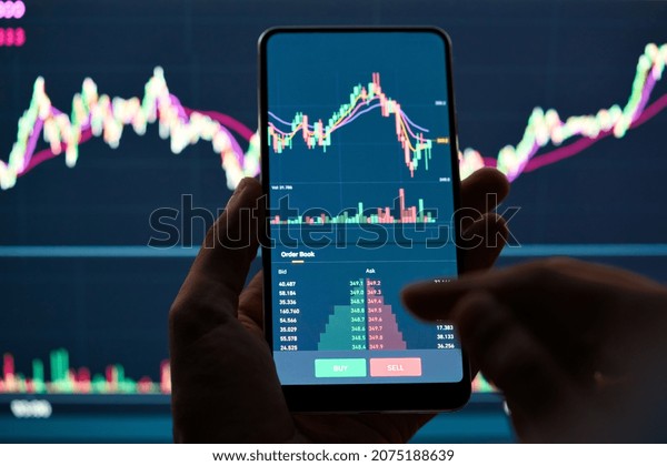 Crypto trader investor broker holding finger\
using cell phone app executing financial stock trade market trading\
order to buy or sell cryptocurrency shares thinking of investment\
risks profit concept.