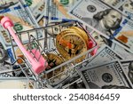 Cryptocurrency golden bitcoin coins in little shopping trolley on US 100 dollars bills background, close up. Digital money and bitcoin concept