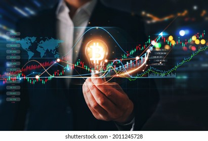 Cryptocurrency Innovation Concept. Businessman Holding Iluminated Light Bulb With  Bitcoin Icon. Increase In Value Of Cryptocurrencies. Futuristic Stock Exchange.
