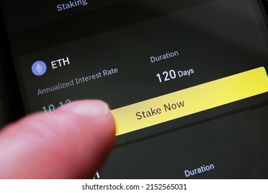 A cryptocurrency investor about to stake Ethereum on a crypto exchange mobile phone app to earn high interest rate. ETH hodler pressing a button to start earning cryptos by staking his holdings. - Shutterstock ID 2152565031