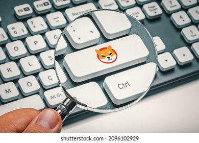 Cryptocurrency trading or exchange concept: Male hand holding magnifying glass and focusing computer key with shiba inu coin logo.