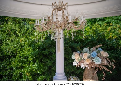 Crystal chandelier luxury style, hanging on the outdoor terrace in the yard. Beautiful classic ceiling lamps and crystals close up. Flowers and greenery in background.