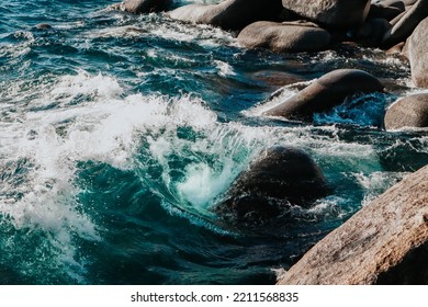 Crystal Clear Blue Lake Wave Crashing Into Large Rocks Forming A Rip Curl With Splashes In Water 