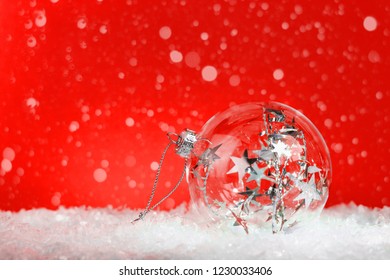 Crystal Clear Glass Christmas Bauble With Silver Tinsel Inside On White Snow: On Red Background With Snow With Copy Space