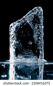 Crystal clear natural ice block in cold blue tones on a black reflective surface. 