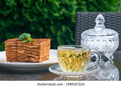 Crystal Cup With Mint Tea, Sugar Bowl And Medovik Cake On Table In Summer Cafe. Tea Drinking Concept, British Culture. Still Life. Lifestyle. Traditional Russian Cuisine, Dessert. Selective Focus.