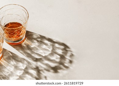 Crystal Glasses with drink, beautiful shadow at sunlight on beige textured background, minimal trend, aesthetic side view shiny glass, sun glare, strong alcohol drink concept, summertime, copy space