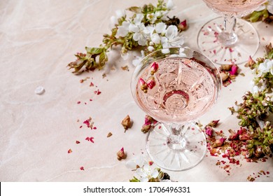 Crystal glasses of pink rose champagne, cider or lemonade with dry rose buds. Blossom cherry branches above. Pink marble background