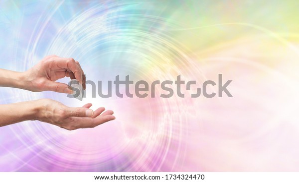 Crystal Healer using clear quartz terminate wand - Female hand pointing a clear quartz terminated crystal into palm of hand against a rainbow coloured spiralling vortex background with copy space 