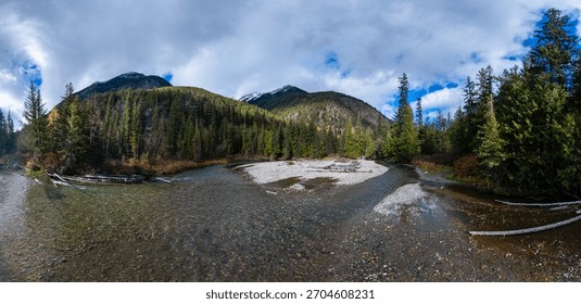 Crystal river winds through a pine forest with mountain peaks in BC, Canada.